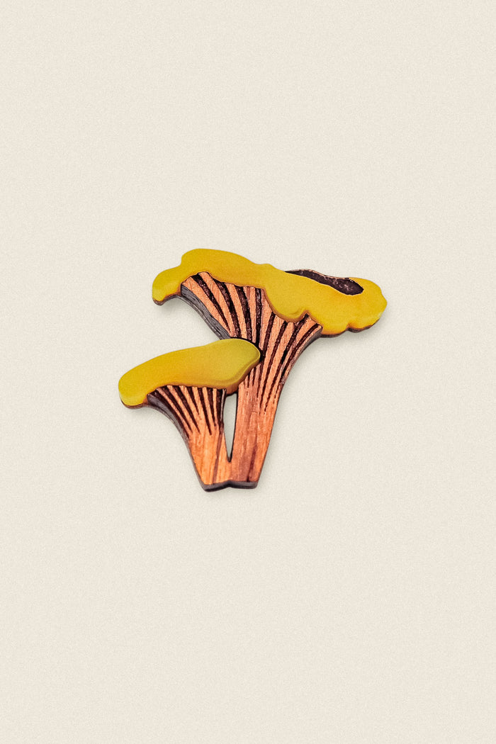 A handcrafted Chanterelle Mushroom Pin, shaped like two golden chanterelles with yellow tops and brown stems, displayed on a plain light background—an eco-friendly accessory for nature lovers.