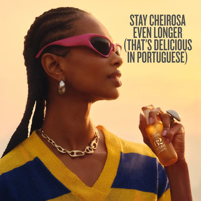 A woman in profile wearing pink sunglasses and a yellow-and-blue striped sweater holds a bottle of R2 Mafik perfume. The image has a warm sunset background and text that reads, 'STAY CHEIROSA EVEN LONGER (THAT'S DELICIOUS IN PORTUGUESE)'.