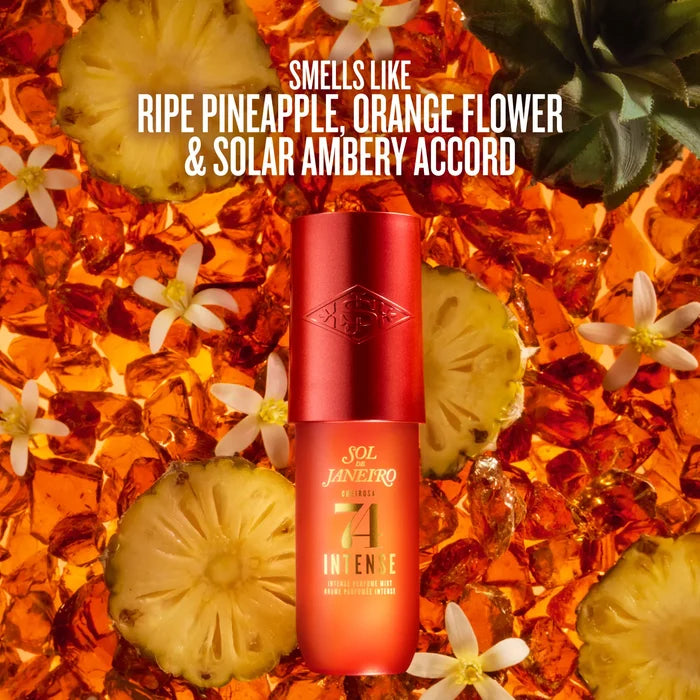 A red and orange cylindrical bottle of Sol Janeiro Intense sunscreen stands centered against a tropical background of sliced pineapple, white flowers, and amber liquid. White text at the top reads, 'SMELLS LIKE RIPE PINEAPPLE, ORANGE FLOWER & SOLAR AMBERY ACCORD.