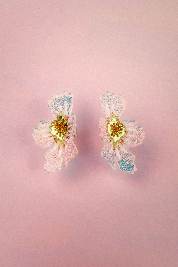 Two pastel pink and purple acrylic flower earrings with gold and white centers are displayed on a light pink background, showcasing their delicate frosted finish. These handmade earrings add a charming floral touch to any ensemble.