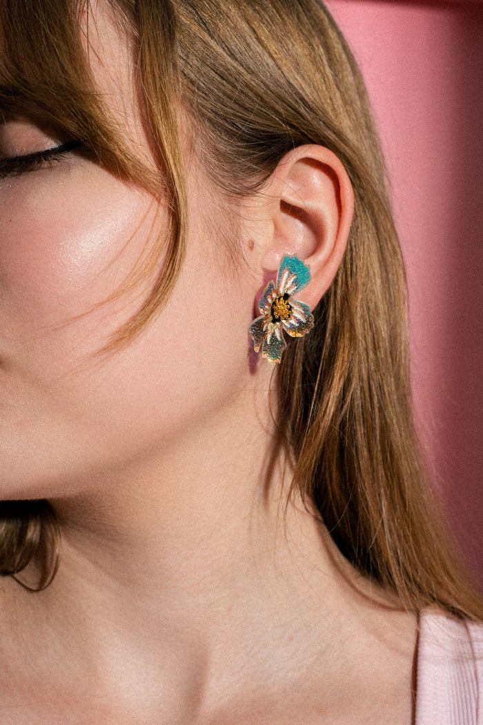 Close-up of a woman’s ear wearing a large, colorful acrylic flower earring. Her light brown hair is partially covering her face, and the background is pink. Only part of her face is visible, highlighting the intricate details of these handmade earrings.