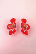 Two red, stylized acrylic flower earrings with white and yellow details are displayed on a light pink background.