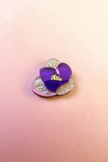 A handcrafted Purple Crocus Flower Lapel Pin, this decorative brooch features pearly cream petals and a translucent purple petal, perfect for nature lovers, set against a soft pink gradient background.