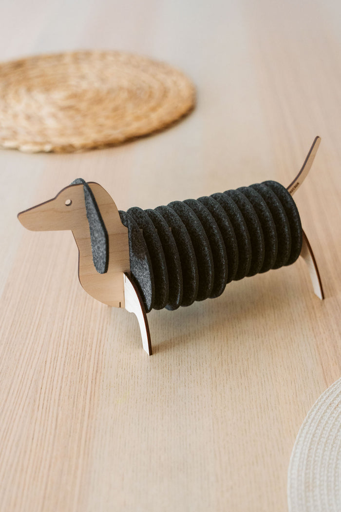 A napkin holder shaped like a dachshund dog, made of wood with black felt napkins forming the dog's body, sits on a light wooden table—perfect for pairing with matching felt coasters or Dachshund coasters for a charming tablescape.
