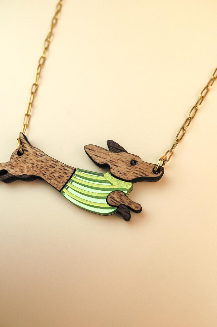 A necklace with a gold chain featuring a Dachshund-shaped pendant, crafted from sustainable wood and wearing a colorful striped sweater.