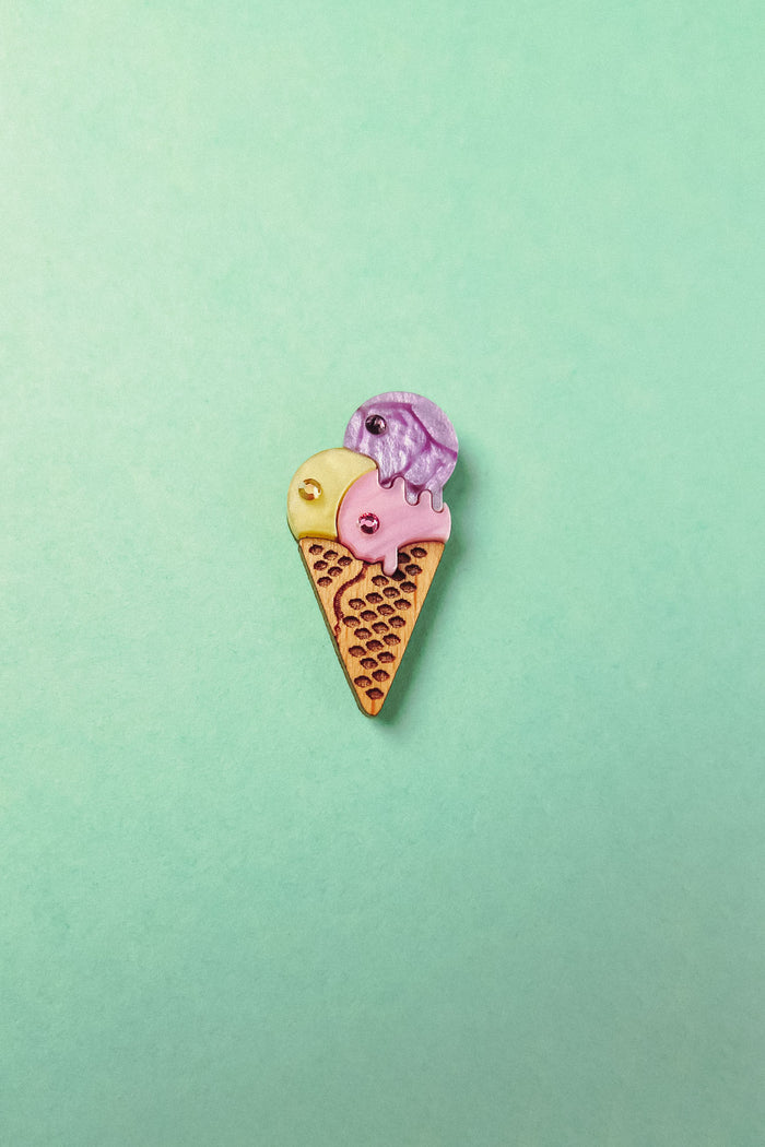 A handcrafted Ice Cream Pin with a playful design features three whimsical scoops—yellow, pink, and purple—on a light green background.