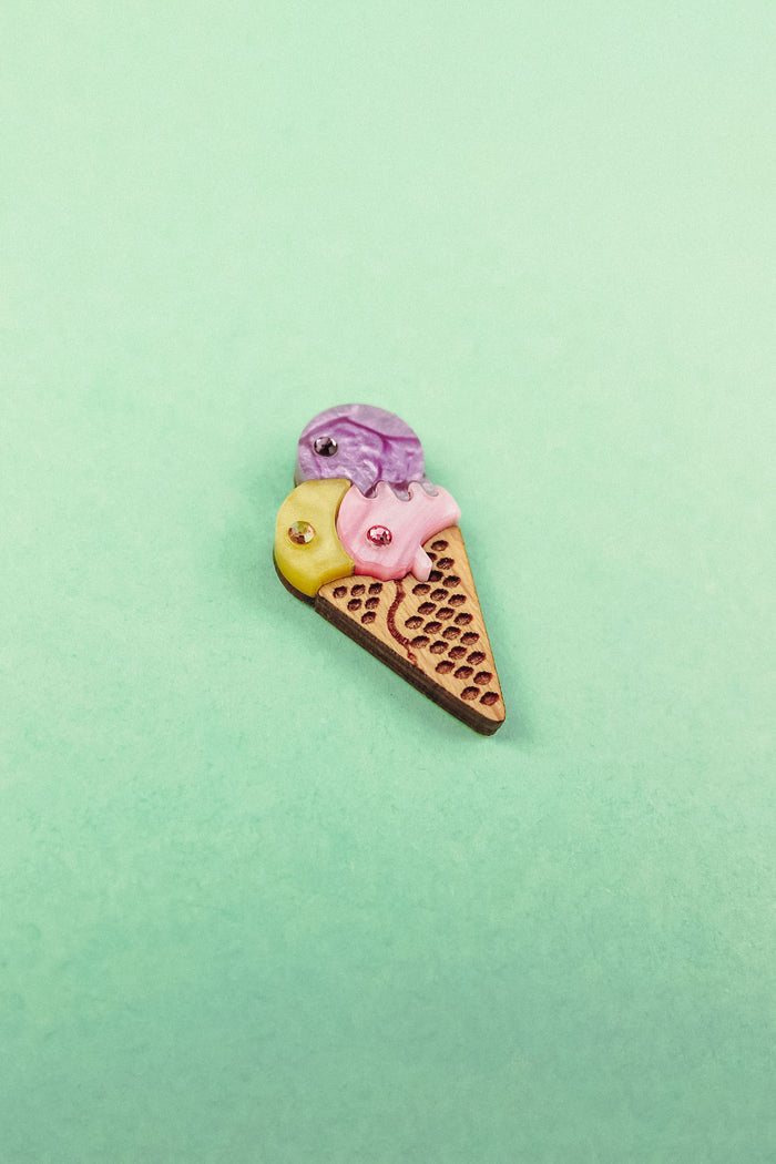 A small, handcrafted Ice Cream Pin with a playful design featuring yellow, purple, and pink scoops topped with gemstone accents, set against a pastel green background.