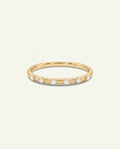 A delicate yellow gold eternity ring featuring five round-cut clear gemstones set in a row, presented on a clean, solid off-white background.