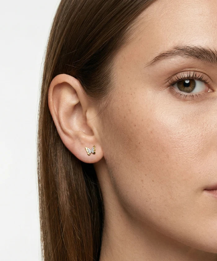 Close-up of a woman wearing butterfly earrings with a plain background