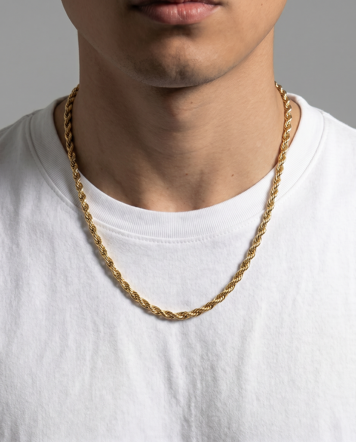 A close-up of a man wearing a gold rope chain necklace over a white crew-neck t-shirt, set against a plain gray background.