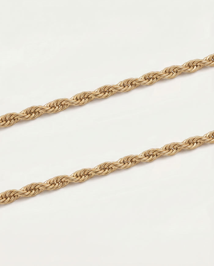 A close-up of a twisted rope chain necklace in a warm gold tone, laid diagonally across a plain white background.