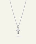 A silver cross pendant necklace on a delicate silver box chain, displayed against a solid off-white background.