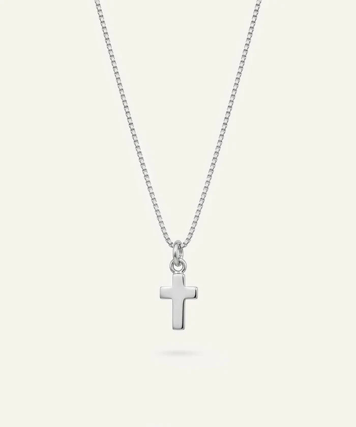 A silver cross pendant necklace on a delicate silver box chain, displayed against a solid off-white background.
