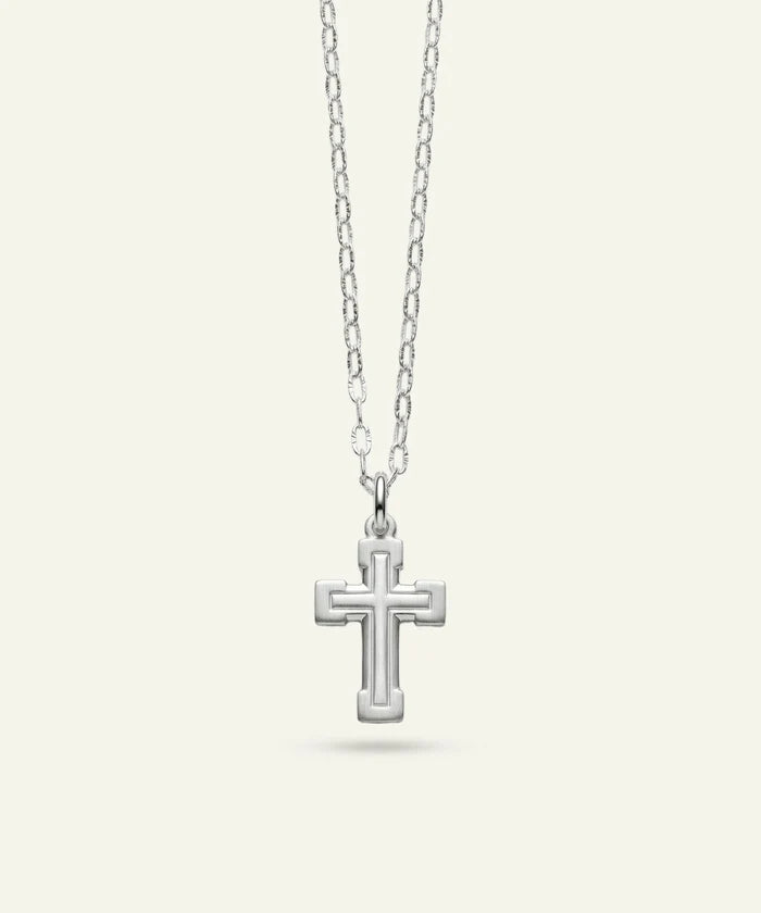 A silver cross pendant necklace with a textured, raised geometric border design, suspended from a delicate silver link chain against a light cream background.