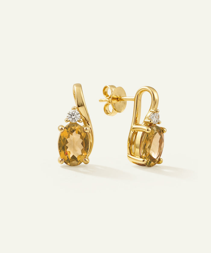 A pair of gold post earrings with oval yellow gemstones and small clear accent stones, shown on a clean off-white background.