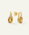 A pair of gold post earrings with oval yellow gemstones and small clear accent stones, shown on a clean off-white background.