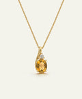 A yellow gold necklace with a curved pendant featuring a large oval-cut yellow citrine gemstone and a small clear accent stone, shown on a light cream background.