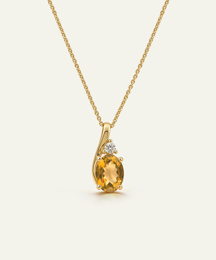 A yellow gold necklace with a curved pendant featuring a large oval-cut yellow citrine gemstone and a small clear accent stone, shown on a light cream background.