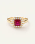 A yellow gold ring featuring a square-cut red ruby center stone surrounded by a halo of small clear stones, with baguette side stones on a clean off-white background.