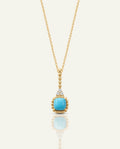 A gold chain necklace featuring a square, light blue turquoise gemstone pendant framed in a beaded gold setting, suspended from a diamond-accented bale, on a plain off-white background.