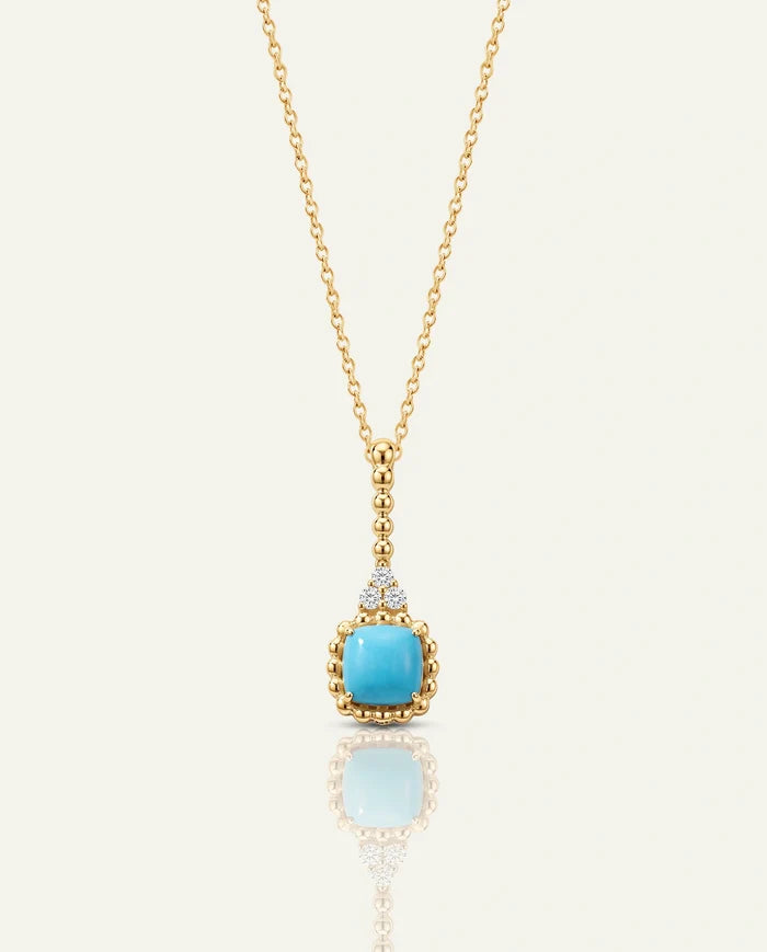 A gold chain necklace featuring a square, light blue turquoise gemstone pendant framed in a beaded gold setting, suspended from a diamond-accented bale, on a plain off-white background.