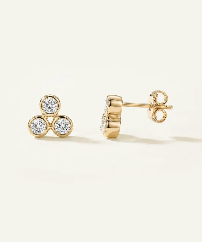 Gold earrings with diamond accents on a light beige background