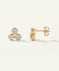 Gold earrings with diamond accents on a light beige background