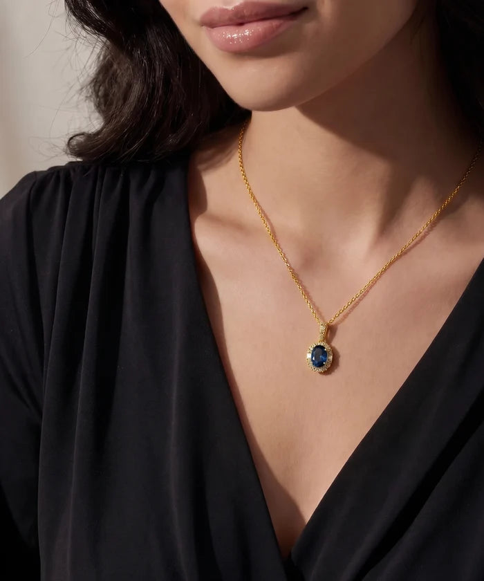 Close-up of a woman wearing a gold necklace with a blue gemstone pendant.