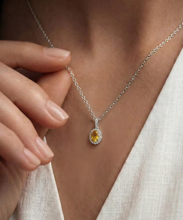 Close-up of a silver necklace with a yellow gemstone pendant on a person wearing a white top.