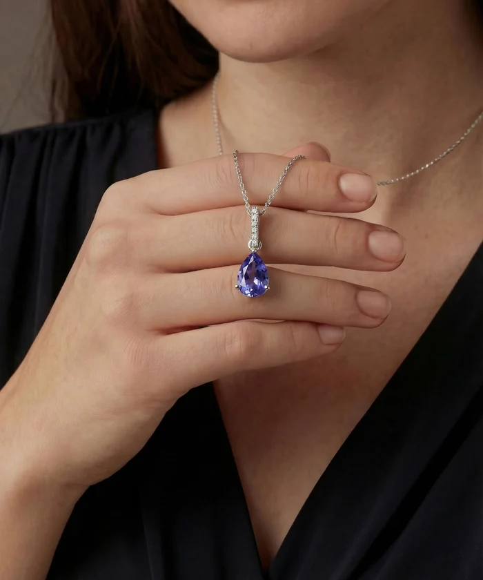 Person wearing a silver necklace with a blue gemstone pendant