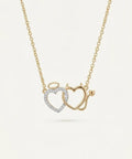 Gold necklace with interlocking heart pendants on a light beige background