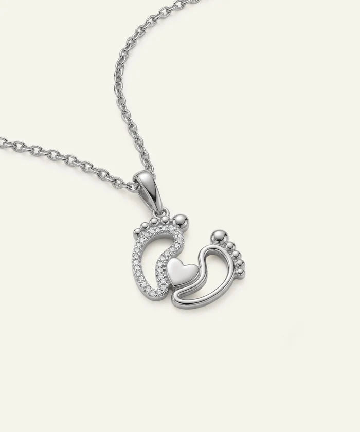 Silver necklace with a pendant featuring two interlocking footprints and a heart on a white background.