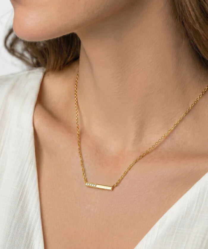 Gold necklace with a heart-shaped pendant worn by a person in a white outfit.