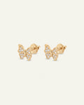 A pair of gold butterfly stud earrings paved with small round clear diamonds, displayed side by side against a light off-white background.