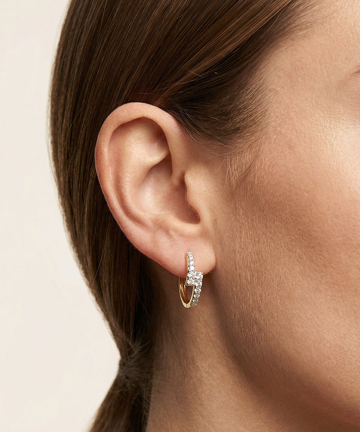 Close-up of an ear wearing a diamond hoop earring on a neutral background