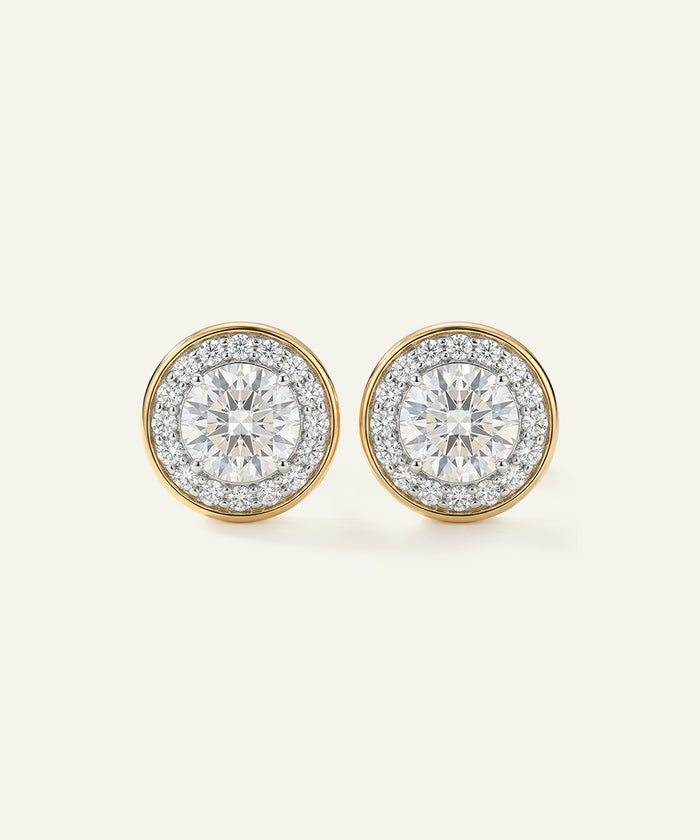 Pair of diamond earrings with gold rims on a light gray background