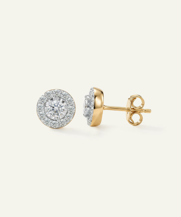 Pair of diamond stud earrings in gold and silver on a light beige background