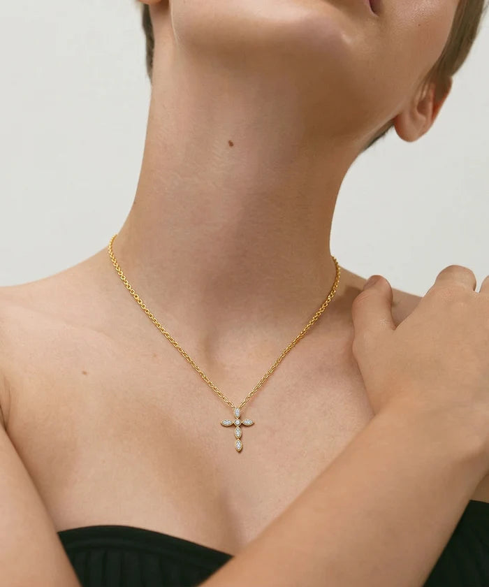Gold necklace with a cross pendant worn by a person against a neutral background