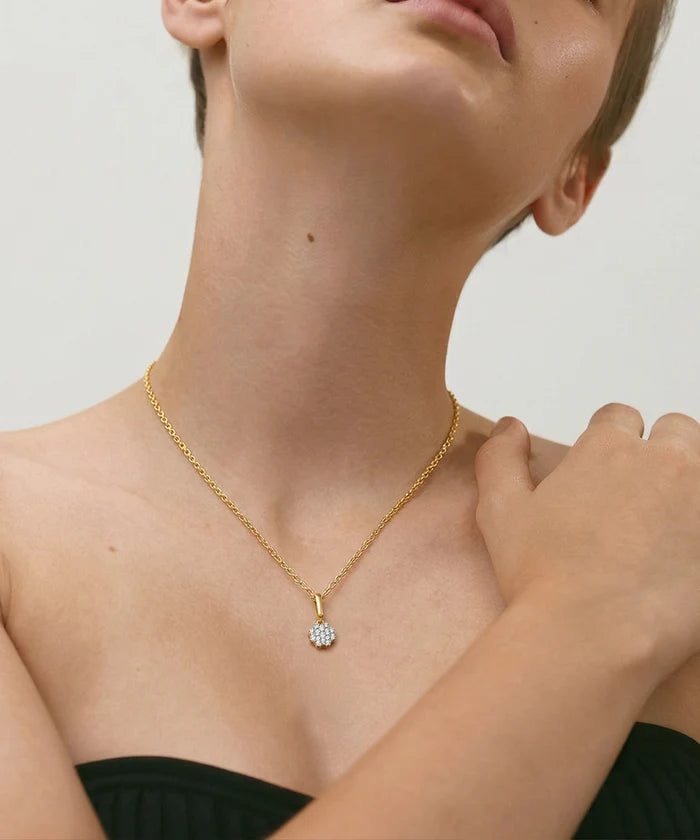 Gold necklace with a diamond pendant worn by a person against a neutral background