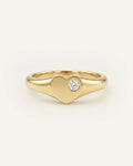 A polished yellow gold heart-shaped ring with a single round-cut clear gemstone set in the center, photographed on a clean off-white background.