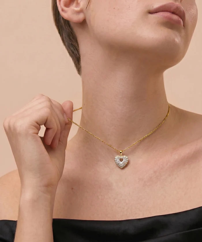 Gold necklace with a heart-shaped pendant worn by a person on a beige background