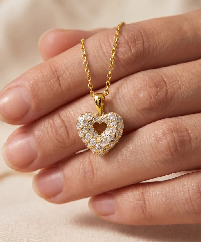 Gold heart-shaped necklace with diamonds held by a hand on a beige background