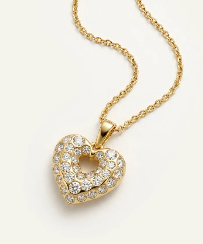 Gold heart-shaped necklace with clear stones on a light beige background
