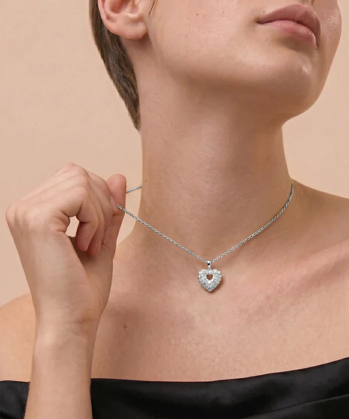 Person wearing a silver heart-shaped necklace against a beige background