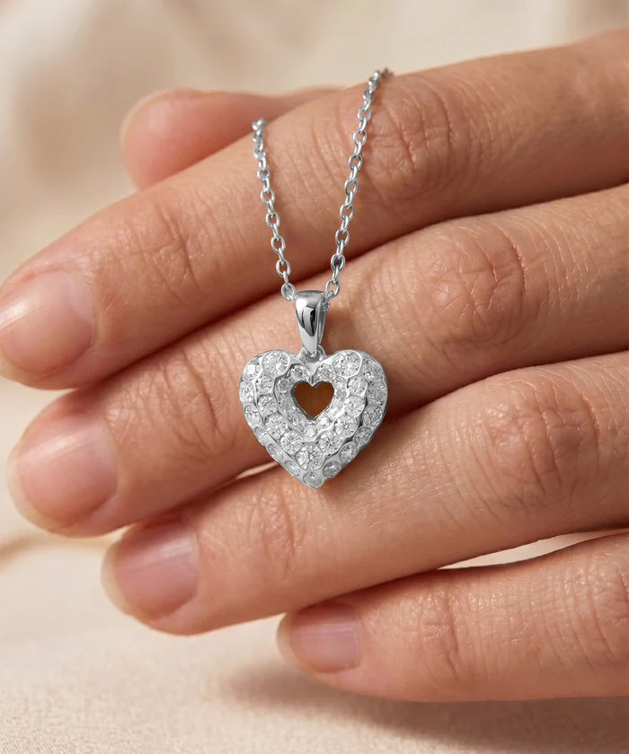 Silver heart-shaped pendant necklace held in a hand against a neutral background