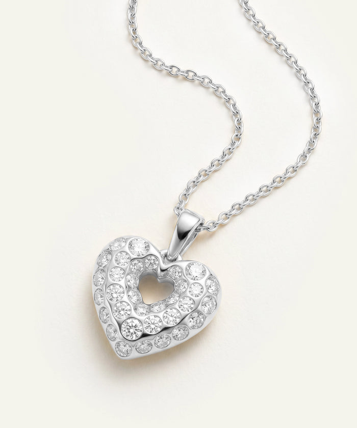 Heart-shaped silver pendant with clear stones on a white background