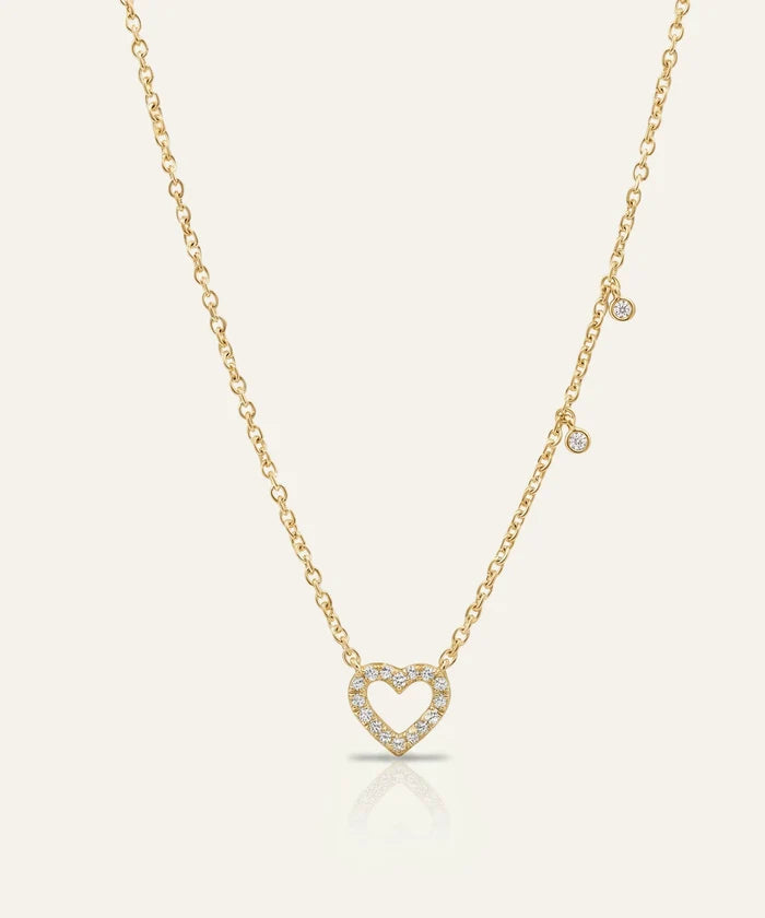 Gold necklace with a heart-shaped pendant on a light beige background