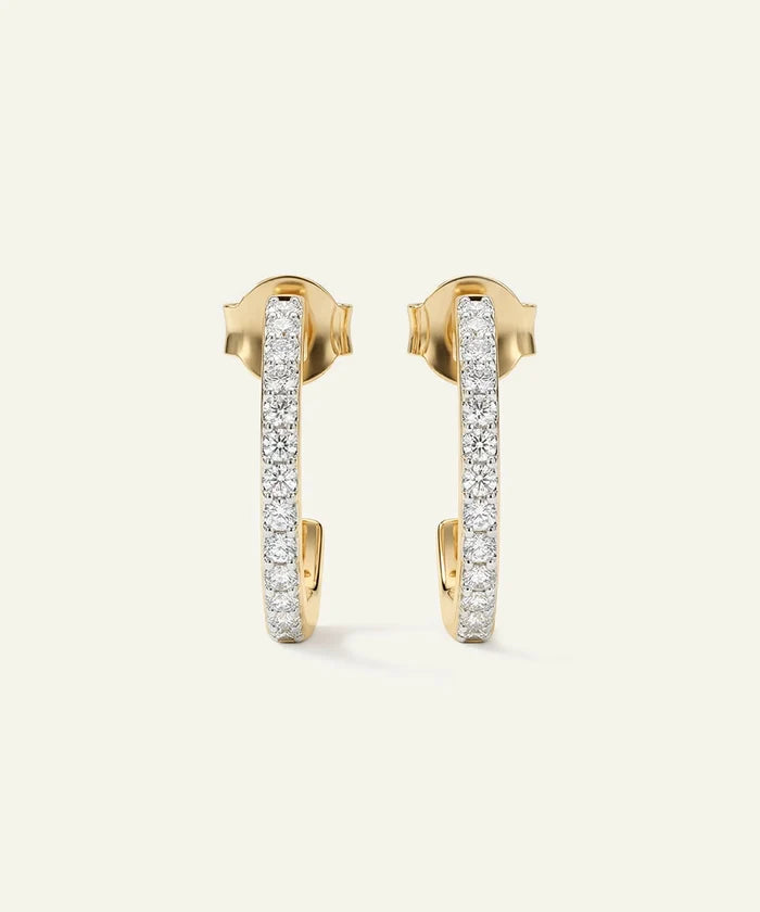 Gold hoop earrings with embedded diamonds on a light beige background