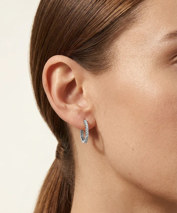 Close-up of a person wearing a silver hoop earring with a light background