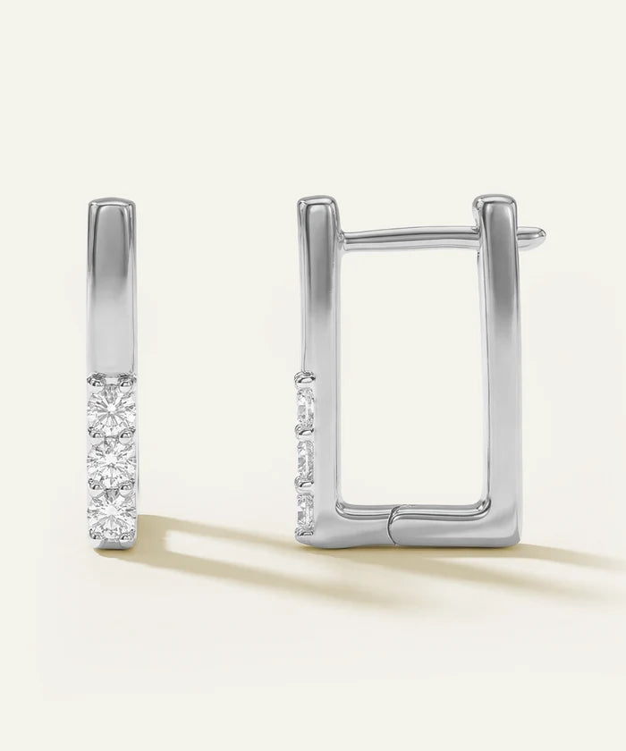 Pair of silver hoop earrings with diamond accents on a light beige background